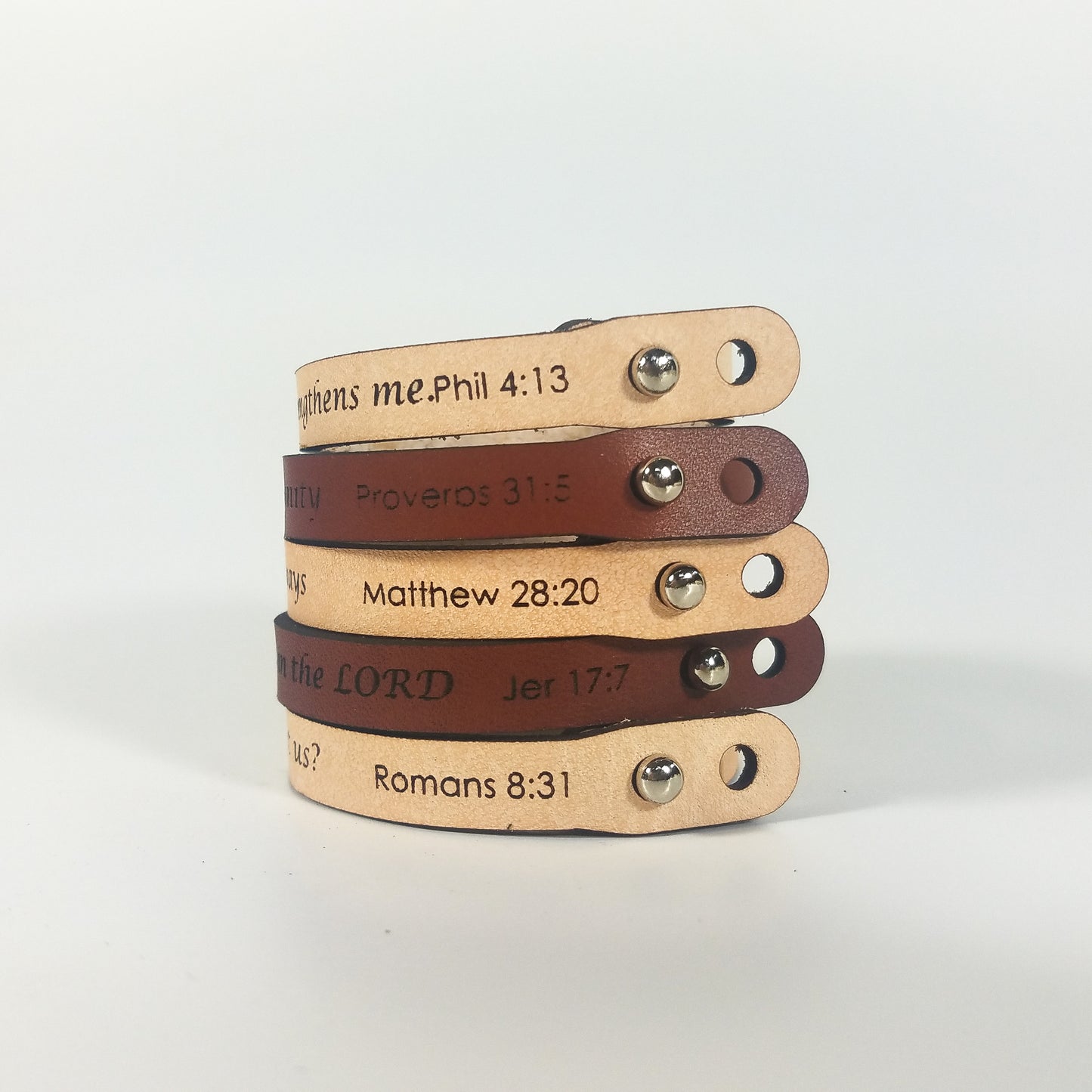 Stack of leather bracelets with engraved text on a light background