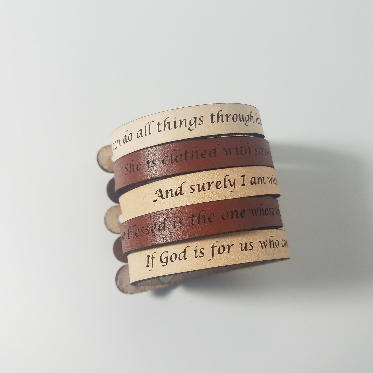 Stack of leather bracelets with engraved text on a light gray background
