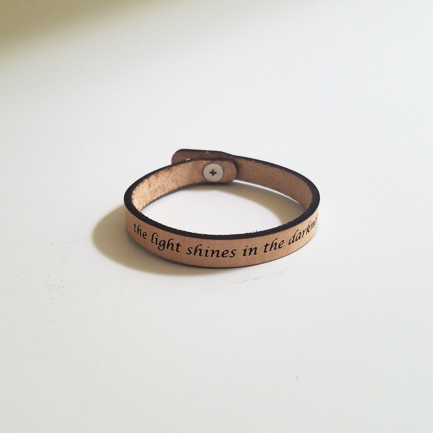 Brown leather bracelet with engraved text on a light beige background