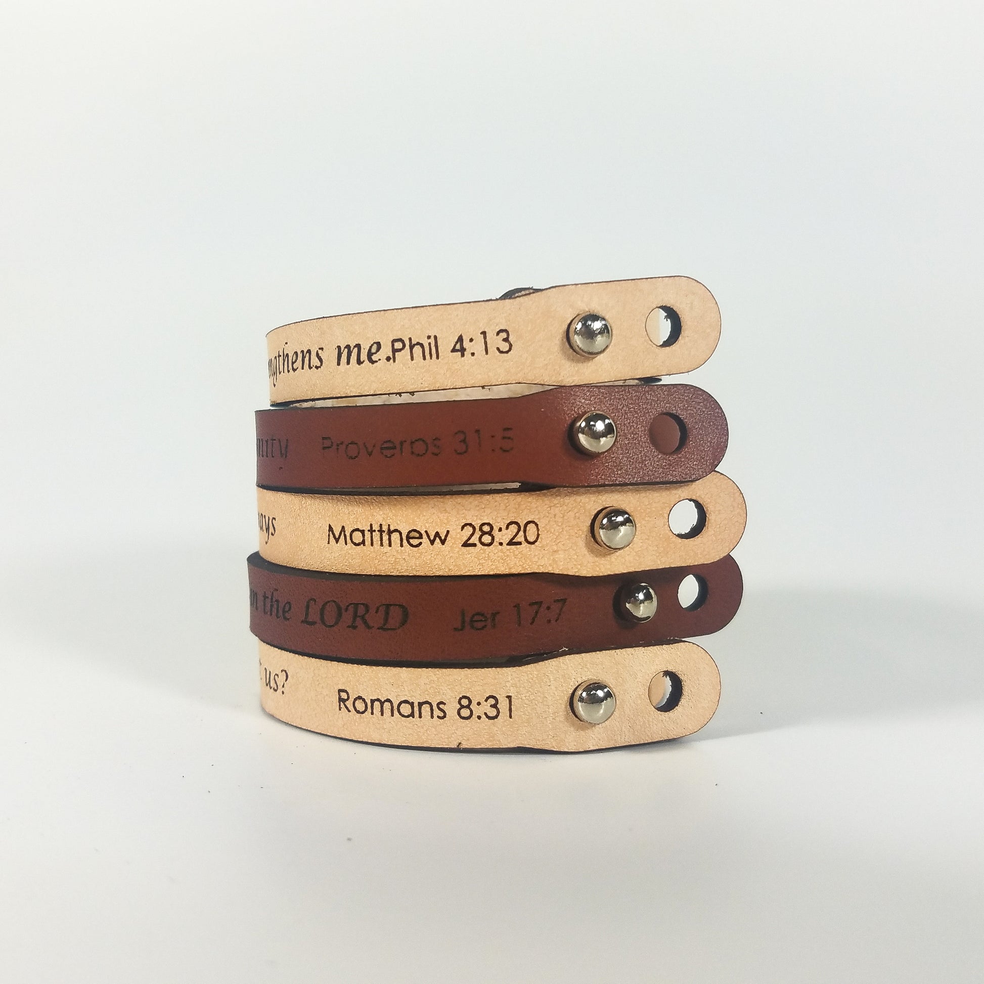 Stack of leather bracelets with engraved text on a light background