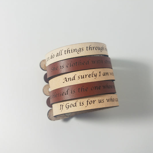 Stack of leather bracelets with engraved text on a light gray background