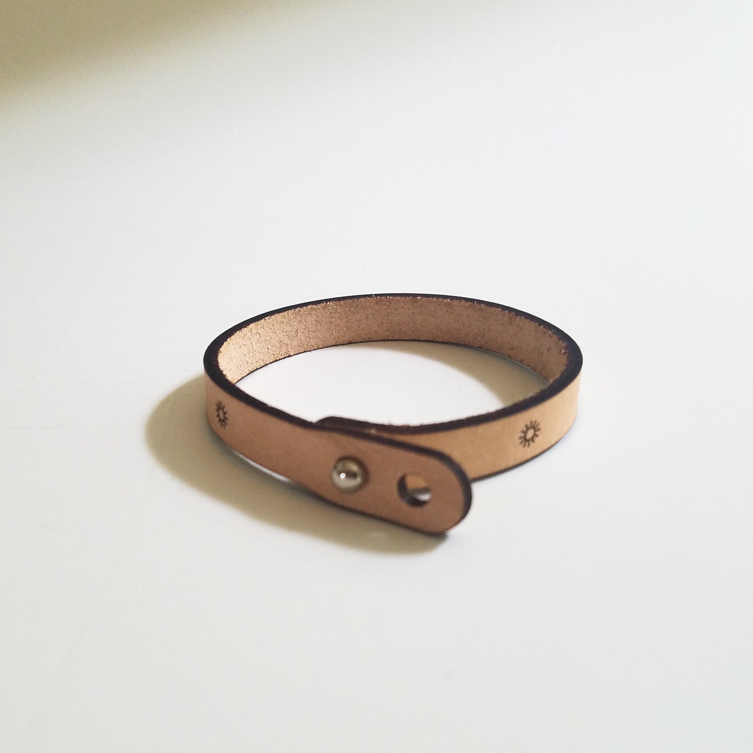 Brown leather bracelet with metal clasps on a light gray background